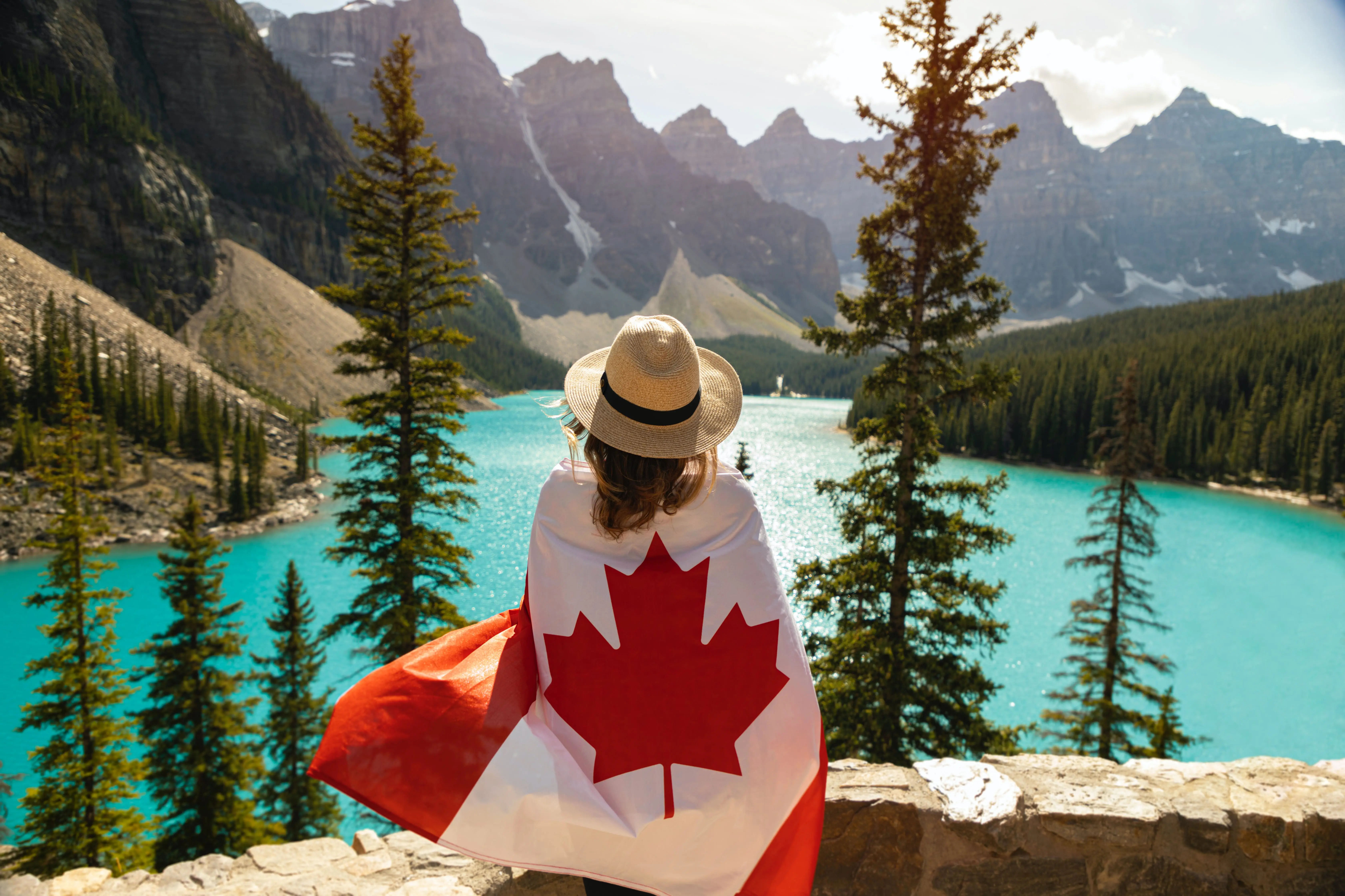 Canadian flag being held behind a woman's body, overlooking the mountains.